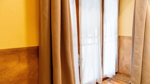 A corner of a room with a wooden floor, beige walls, and a window with white curtains.