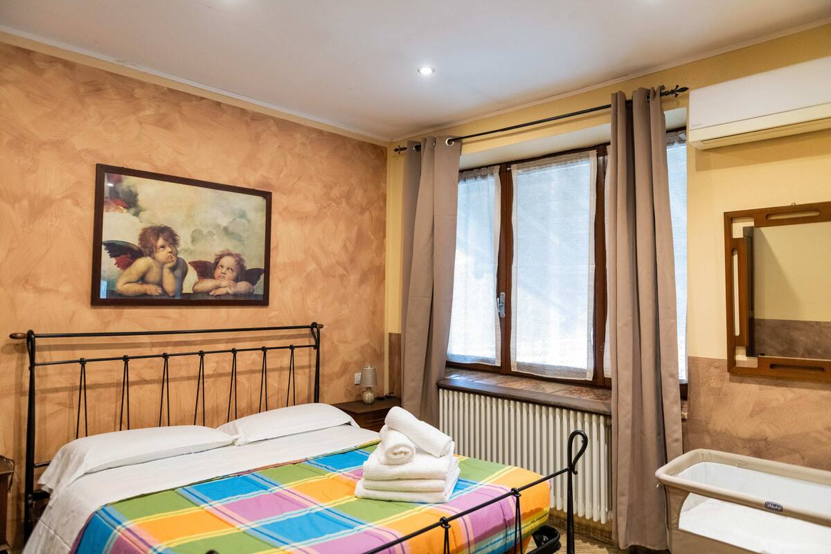 Een slaapkamer met een bed, een radiator, een raam met gordijnen en een schilderij aan de muur.