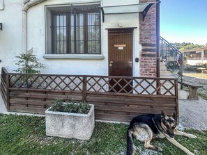 Edificio con cerca de madera, puerta y pequeño jardín con un perro.