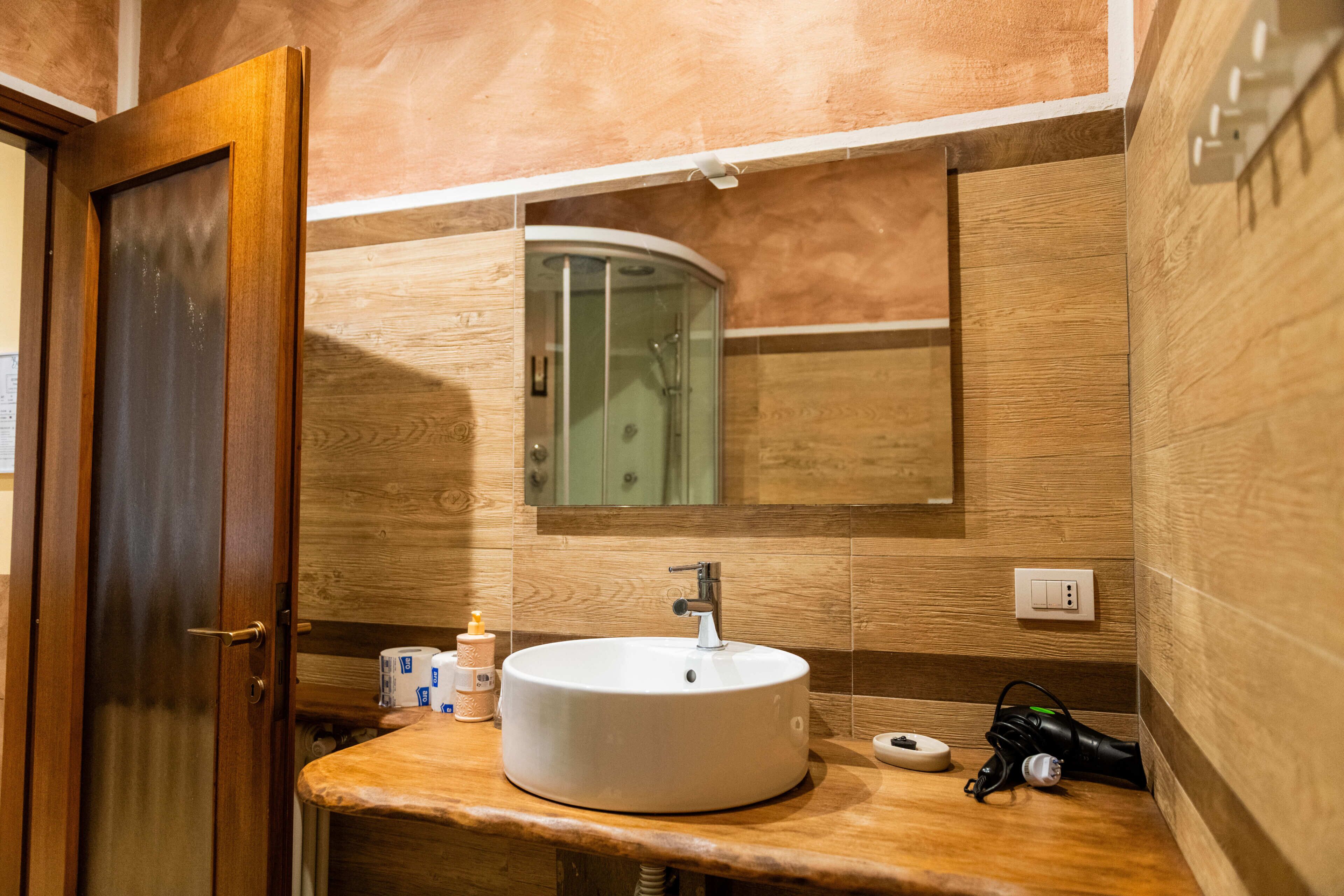 A bathroom with a wooden vanity, a sink, a mirror, and a shower.