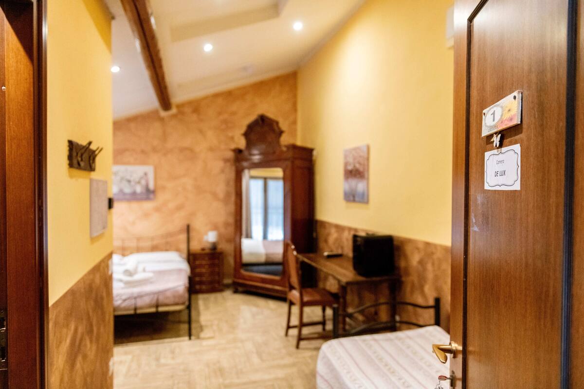 Een hotelkamer met een bed, een bureau, een stoel, een spiegel en een deur met een bordje.