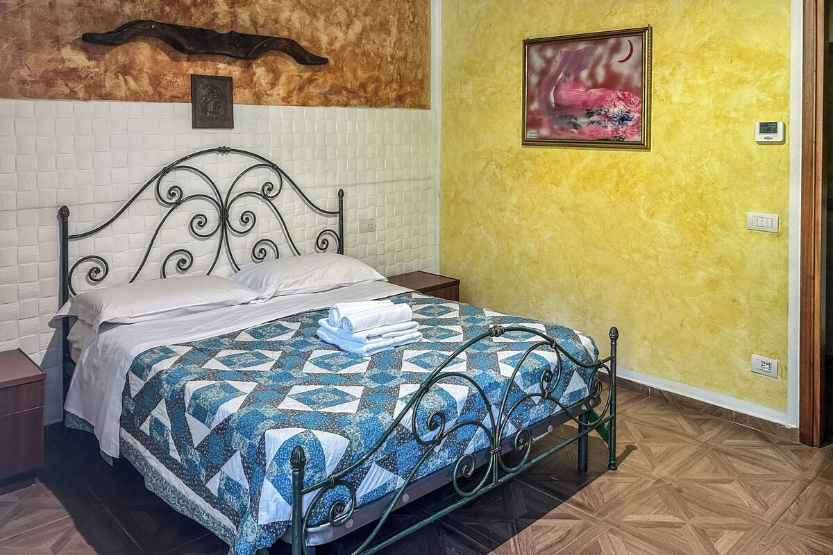 Een bed met een gebedruid sprei, een wandklok en een ingelijst schilderij aan de muur.