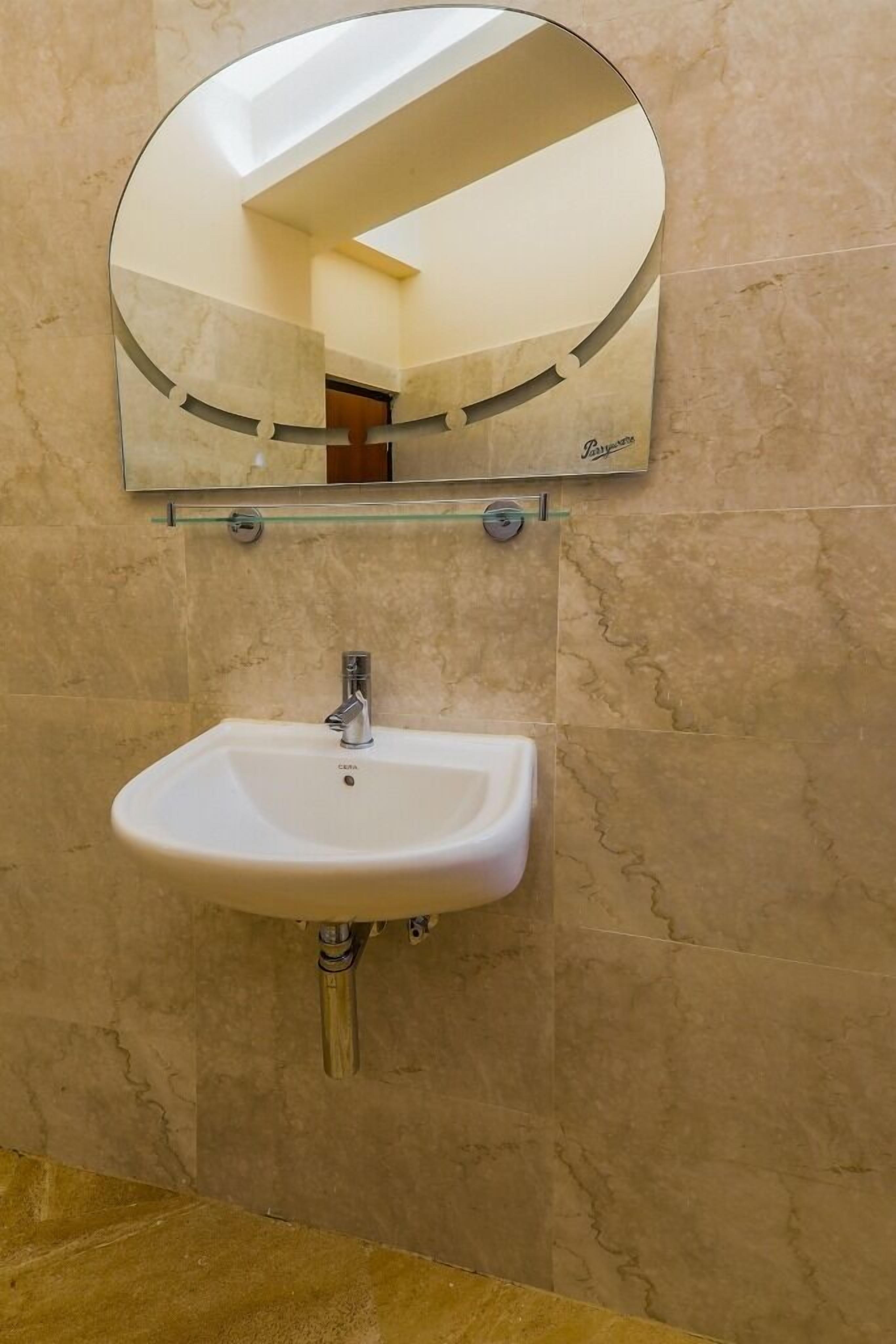 A bathroom with a white sink, a glass shelf, and a mirror.