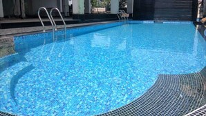 A swimming pool with clear blue water, metal ladders, and a tiled edge. - Airport Guest House Guwahati (Guwahati)