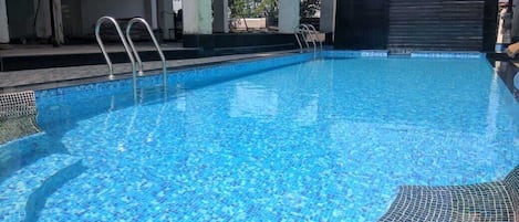 A swimming pool with clear blue water, metal ladders, and a tiled edge.
