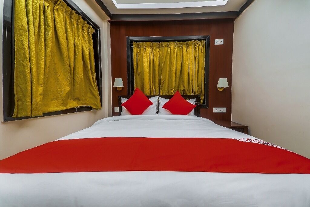 Habitación de hotel con cama, dos almohadas rojas, colcha roja y blanca, y un tragaluz sobre la cama.