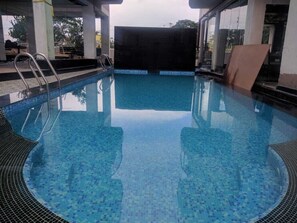 Una piscina con agua cristalina, escaleras de metal y un borde con azulejos.