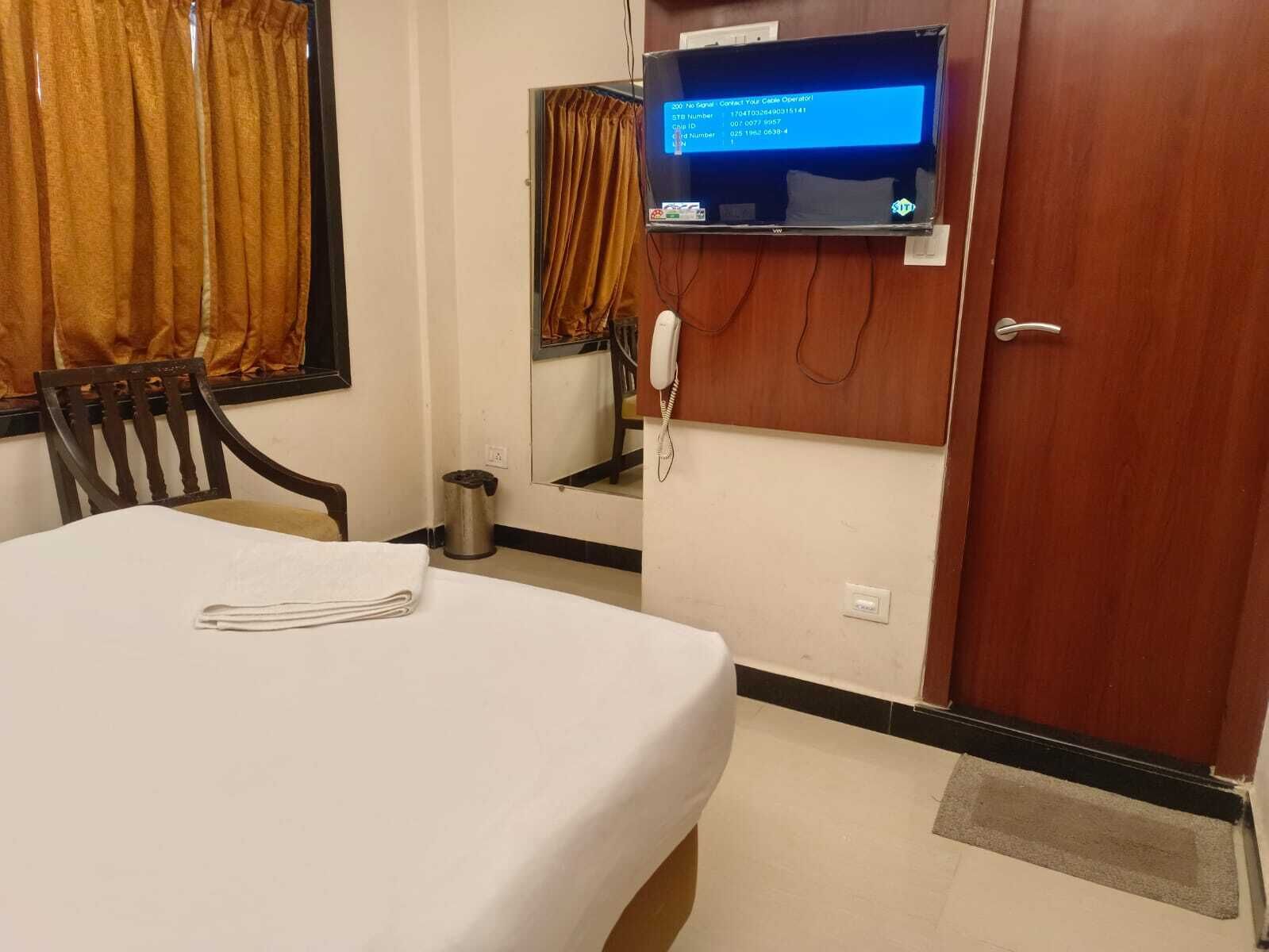 A hotel room with a bed, a desk, a chair, a telephone, and a television mounted on the wall.