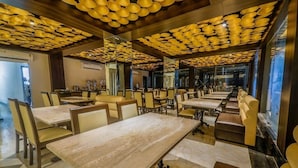 A restaurant with multiple tables and chairs, a marble floor, and a ceiling with a patterned design. - Airport Guest House Guwahati (Guwahati)