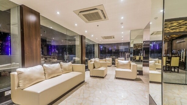 A modern hotel lobby with a marble floor, a large beige sofa, and multiple armchairs. - Airport Guest House Guwahati (Guwahati)