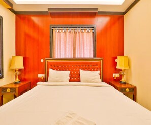 Habitación de hotel con una cama grande, dos mesitas de noche con lámparas, un cabecero de madera y una ventana con cortinas.