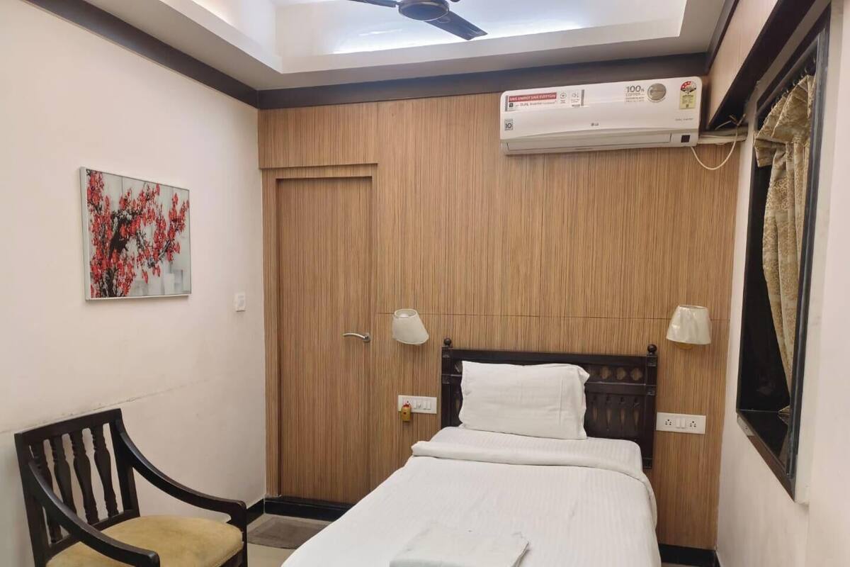 Ein Hotelzimmer mit einem Bett, einem Sessel, einem Deckenventilator, einer Klimaanlage und einem Bild an der Wand.