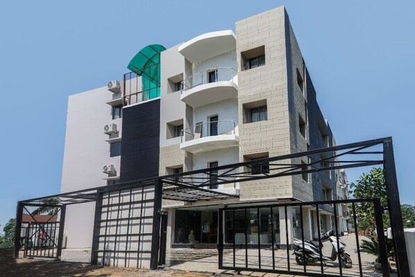 Un edificio de varios pisos con entrada protegida por un portón, un área techada y una moto estacionada.