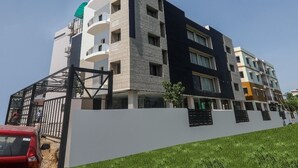 A multi-story residential building with balconies, a gated entrance, and a white wall in the foreground. - Airport Guest House Guwahati (Guwahati)