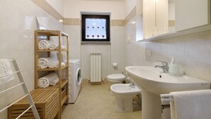 A bathroom with a washing machine, toilet, bidet, and a shelf with towels. - Studio 'Como's Lake Mountains Beb' with Mountain View, Private Terrace & Wi-Fi (Cremeno)