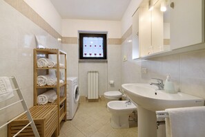 Ein Badezimmer mit Waschmaschine, Toilette, Bidet und einem Handtuchregal.