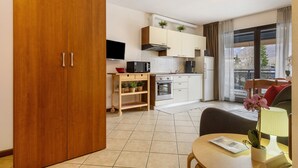 A modern kitchen with a wooden door, a dining area with a table and chairs, and a view of the outside through a large window. - Studio 'Como's Lake Mountains Beb' with Mountain View, Private Terrace & Wi-Fi (Cremeno)