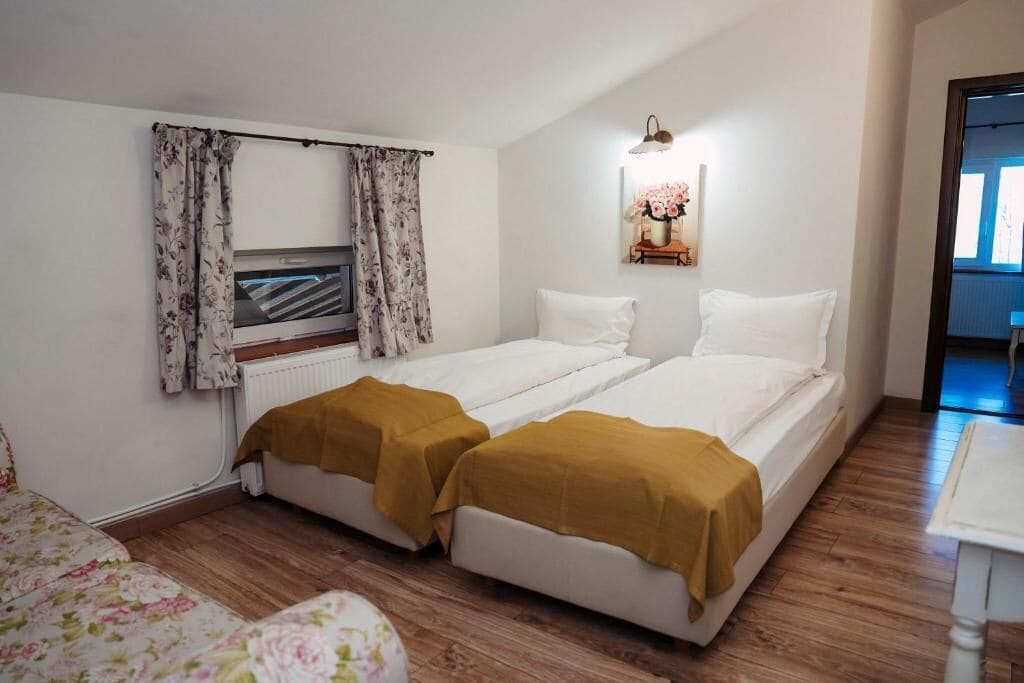 Habitación doble con dos camas, un radiador, una ventana con cortinas y un cuadro en la pared.