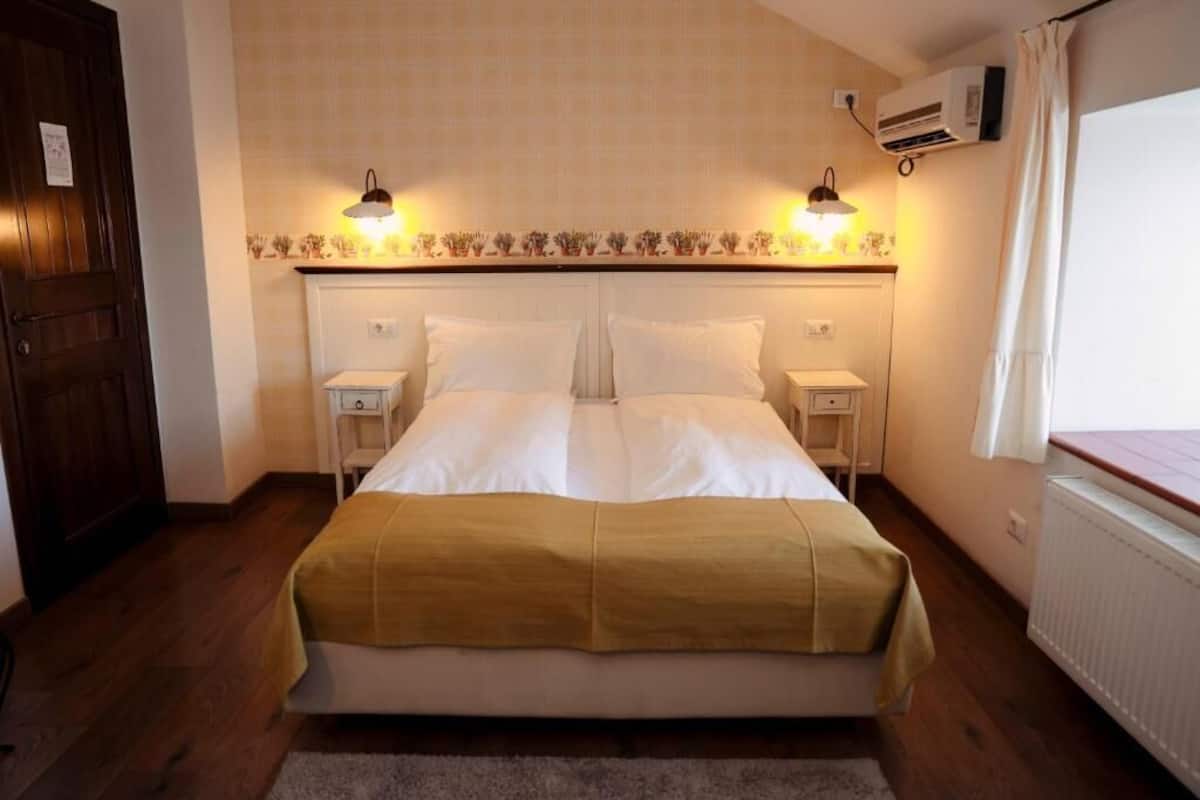 A bedroom with a bed, two bedside tables, a nightstand, a radiator, and an air conditioning unit.