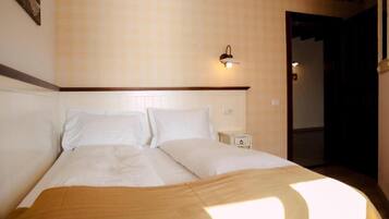 A neatly made bed with white linens, a bedside table with a lamp, and a wall-mounted light fixture.