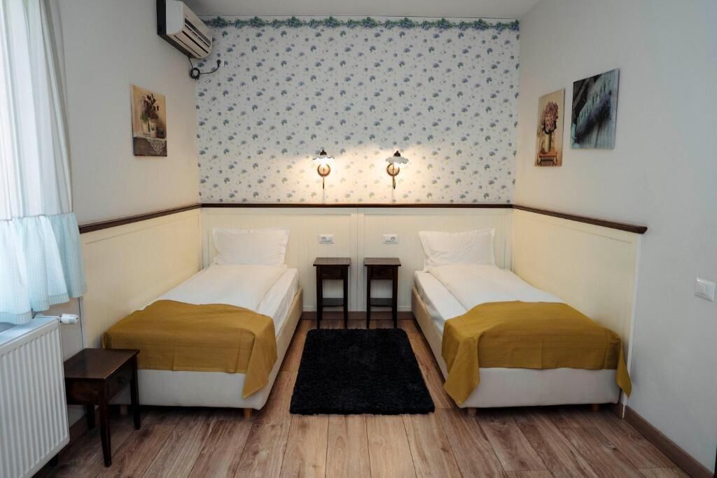A room with two single beds, a black rug, and a floral wallpaper pattern.
