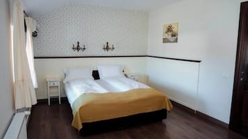 Ein Schlafzimmer mit einem Bett, zwei Nachttischen, einem Heizkörper, einer Wand mit ornamentalem Tapetenmuster und einer Tür.