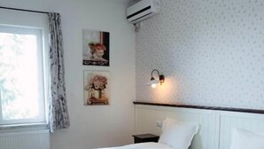Camera d'albergo con due letti, una finestra con tende, condizionatore d'aria, comodino e illuminazione a parete.