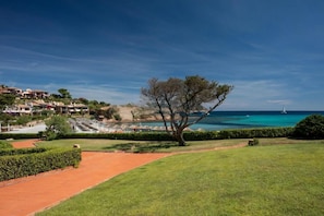 A coastal view with a clear sky, a tree-lined pathway, and a sailboat on the water. - Elite Collection Villa Pevero Acquamarina (Porto Cervo)