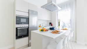 Uma cozinha moderna com forno embutido, micro-ondas e frigorífico, uma bancada de refeições com assentos e uma grande janela que proporciona luz natural.