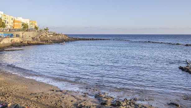 Uma praia costeira com edifícios, linha costeira rochosa e mar calmo.