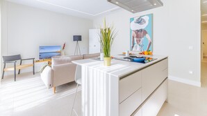 Uma cozinha moderna com uma ilha central, uma área de refeições com sofá e mesa, e uma televisão ao fundo.