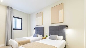 Quarto de hotel com duas camas, uma janela com cortinas e dois espelhos fixados na parede.