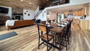 A spacious living area with a wooden ceiling, a fireplace, a sofa, and a dining table with chairs. - Woods + Water Retreat (Lac du Flambeau)