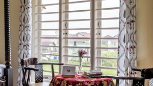 Ein Zimmer mit großem Fenster, einem Tisch mit Laptop, Büchern und einer Vase mit Blumen.