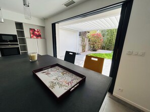 A modern kitchen with a dining area, a TV, and a view of the garden. - Spacious modern villa with garage (La Grande-Motte)