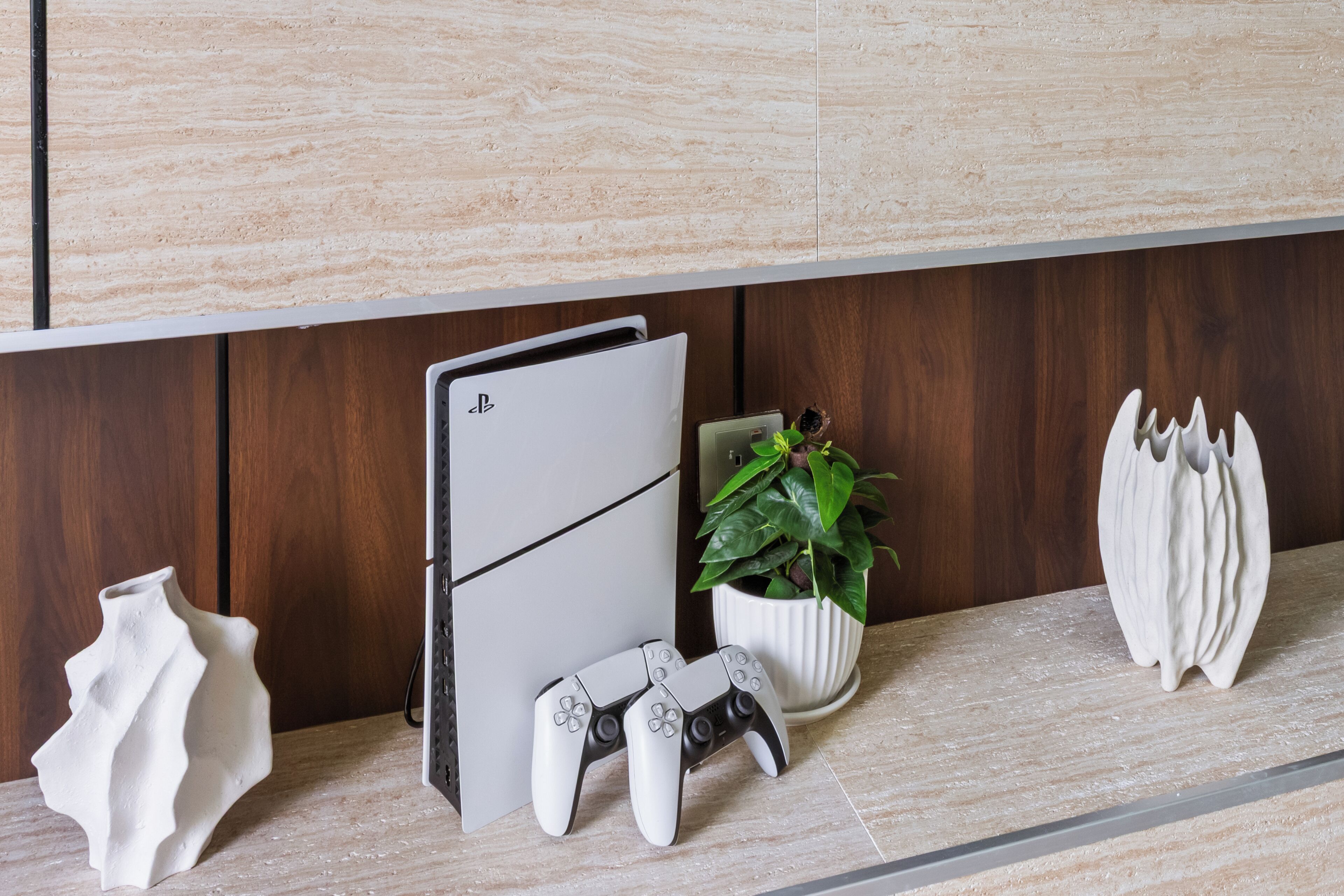 A kitchen counter with a PlayStation 5, a white vase, a potted plant, and a decorative item.