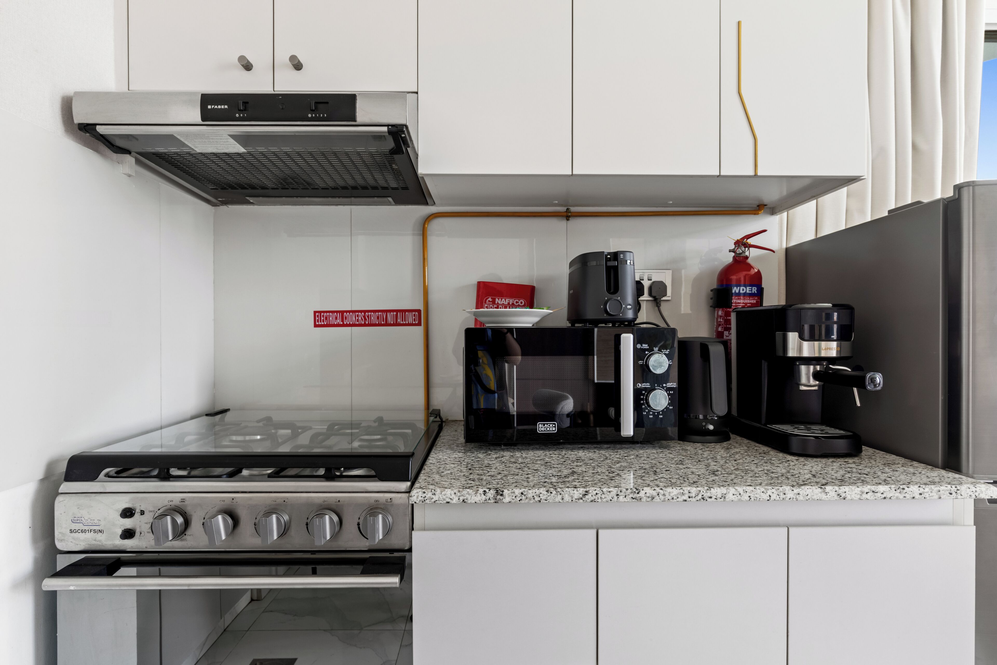 A kitchen with a gas stove, microwave, coffee maker, and a fire extinguisher.