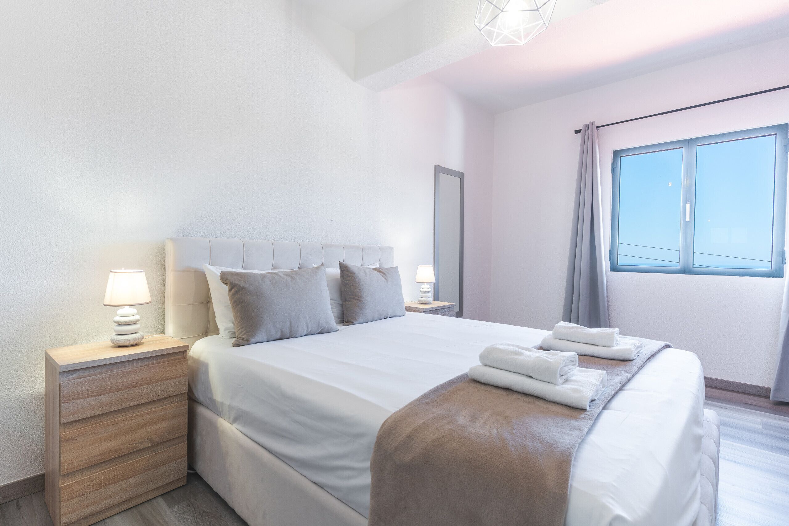 Una habitación de hotel con cama, mesitas de noche, ventana y vista al cielo.