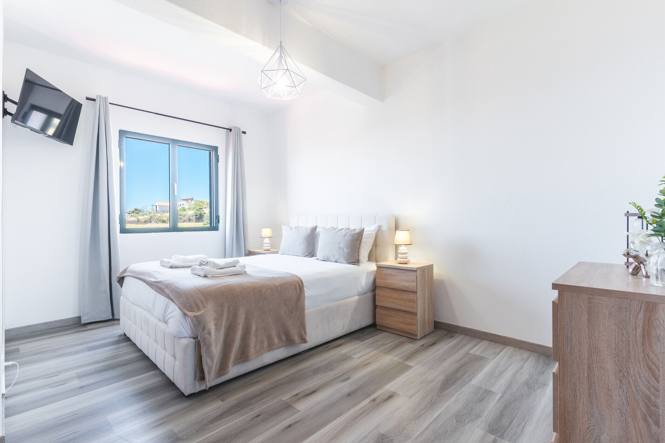 A hotel room with a bed, bedside tables, a TV mounted on the wall, and a window with curtains.