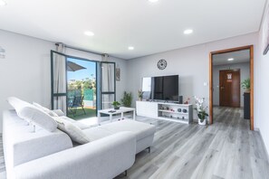 A modern living room with a sofa, TV, and a view to the outside. - StarFish Apartment by Atlantic Holiday (Calheta)