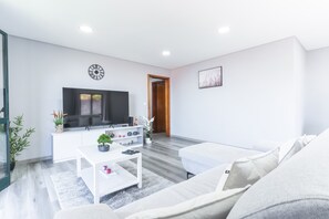 A modern living room with a flat-screen TV, a white sofa, a coffee table, and a small side table with decorative items. - StarFish Apartment by Atlantic Holiday (Calheta)