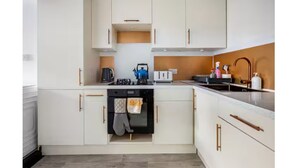 Una cocina moderna con armarios blancos, un lavavajillas negro, una tetera y un tostador.