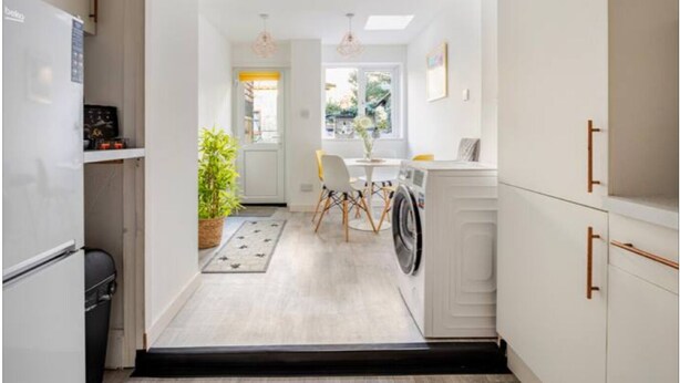 Una cocina estrecha con lavadora, una zona de comedor con mesa y sillas, y una planta en maceta.