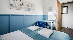 Un dormitorio con cama, un cuadro, un escritorio y una ventana.