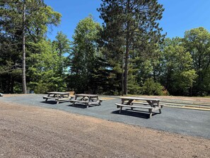 A campground with picnic tables and a gravel parking area surrounded by trees.