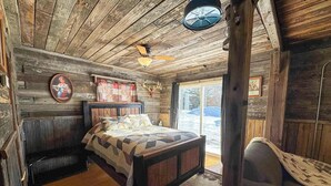 Um quarto rústico de madeira com uma cama, um banco e uma janela grande.