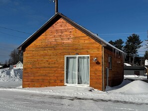 Une petite cabane en bois avec un toit en pente, une porte-fenêtre coulissante et un petit espace porche.