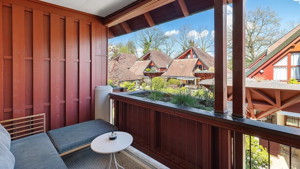 Un balcon avec des balustrades en bois, un banc rembourré et une petite table.