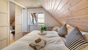 Une chambre avec un plafond en pente, un lit avec des oreillers, une plante et une fenêtre.