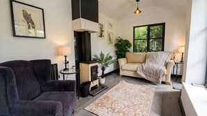 A cozy living room with a fireplace, two sofas, a rug, and a large window. - Tranquil cottage stay with fireplace and pond (Oswestry)
